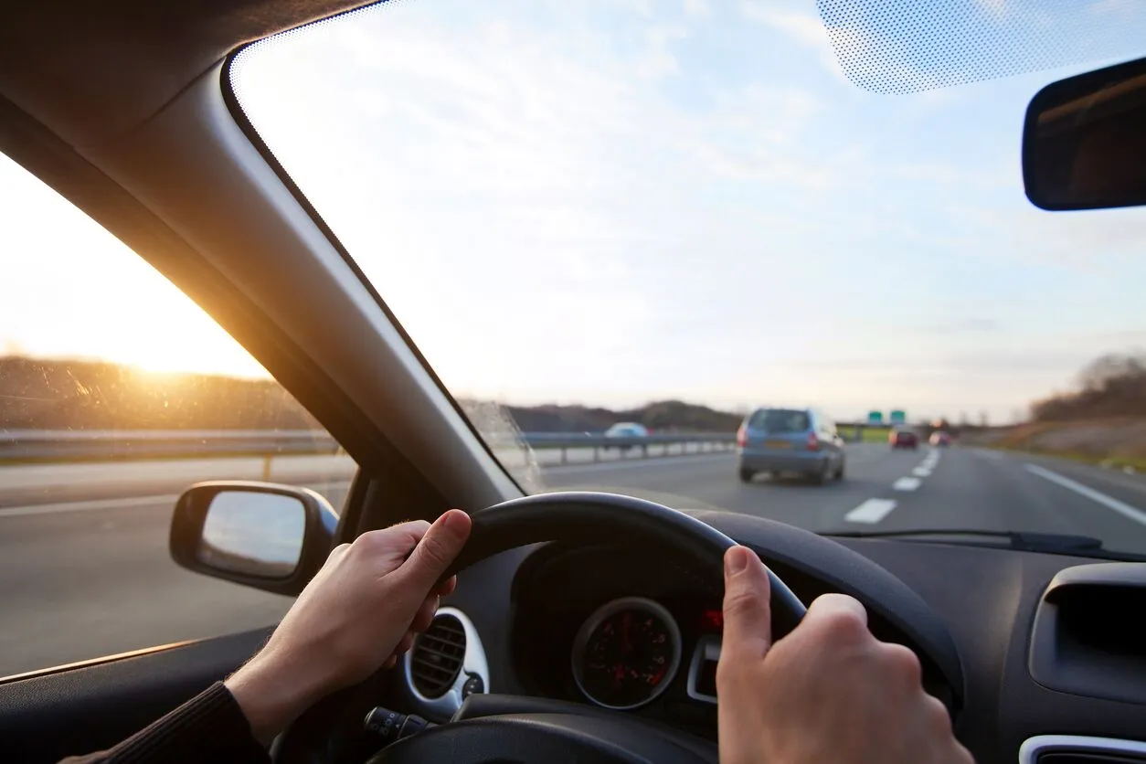 Driver's hands on steering wheel, sunset highway view.