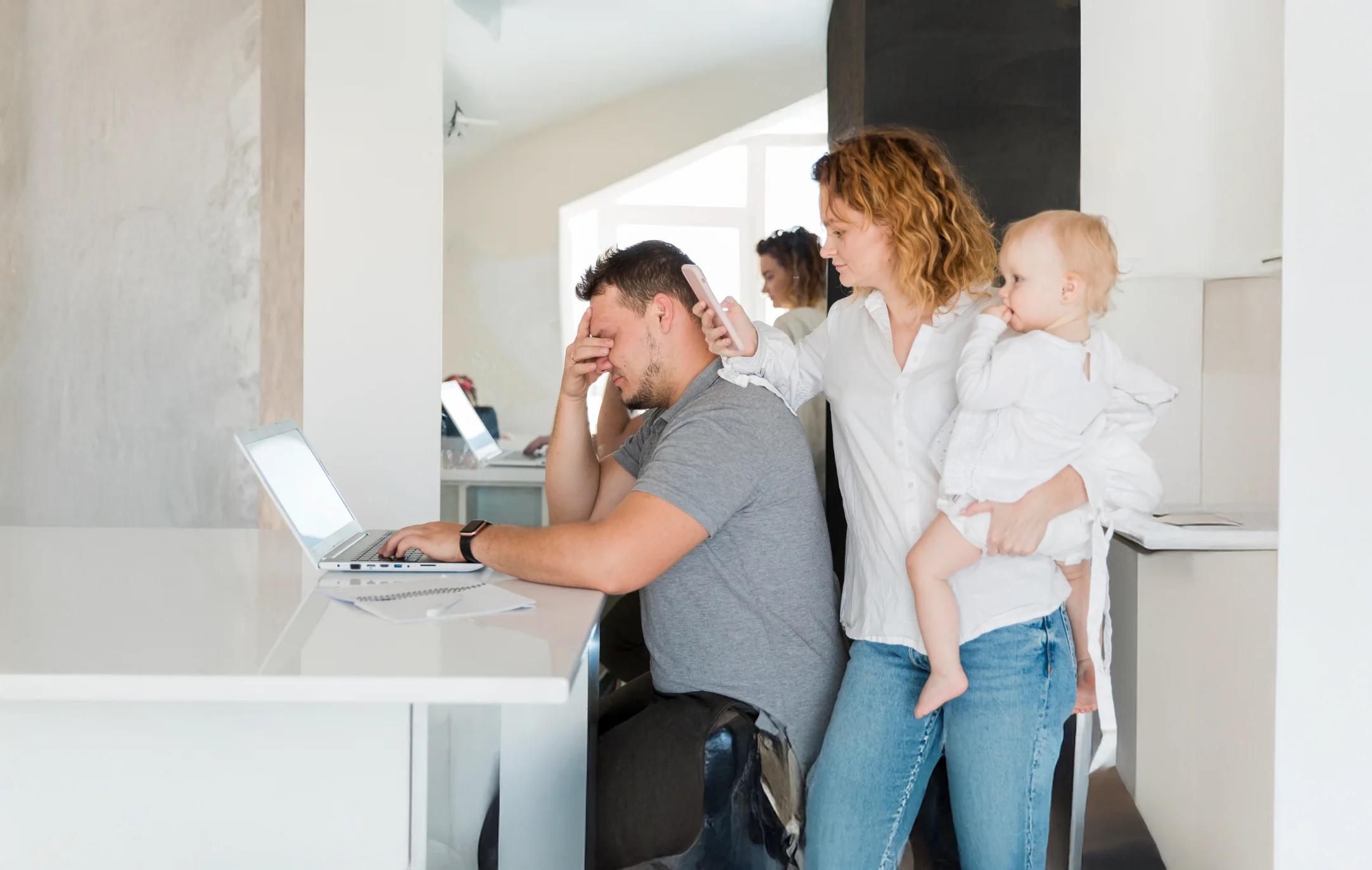 Frustrated parent working on laptop with child nearby.